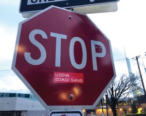 stop sign with sticker reading "using comic sans" in comic sans font