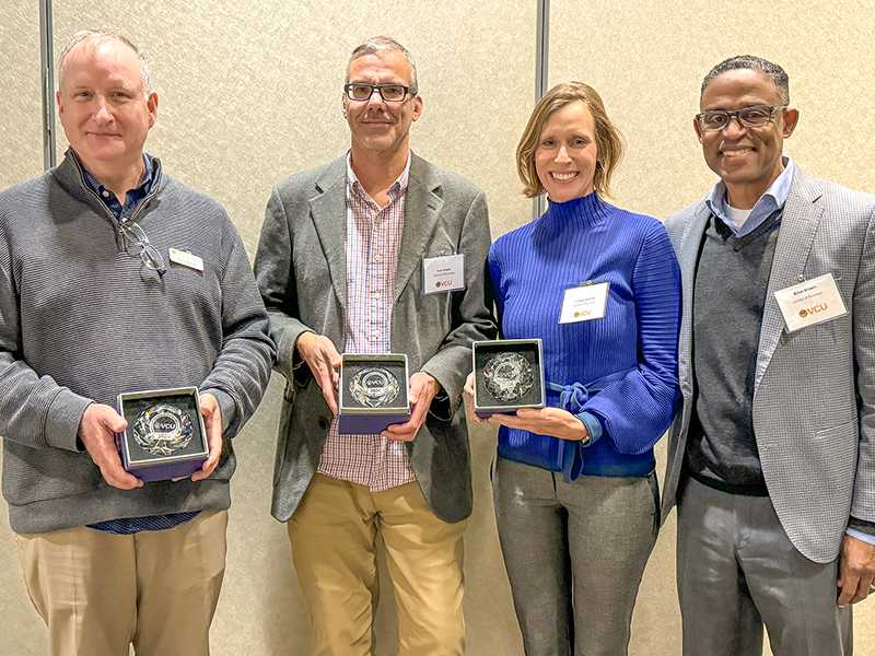 four individuals standing side by side, smiling, while holding crystal awards in presentation boxes