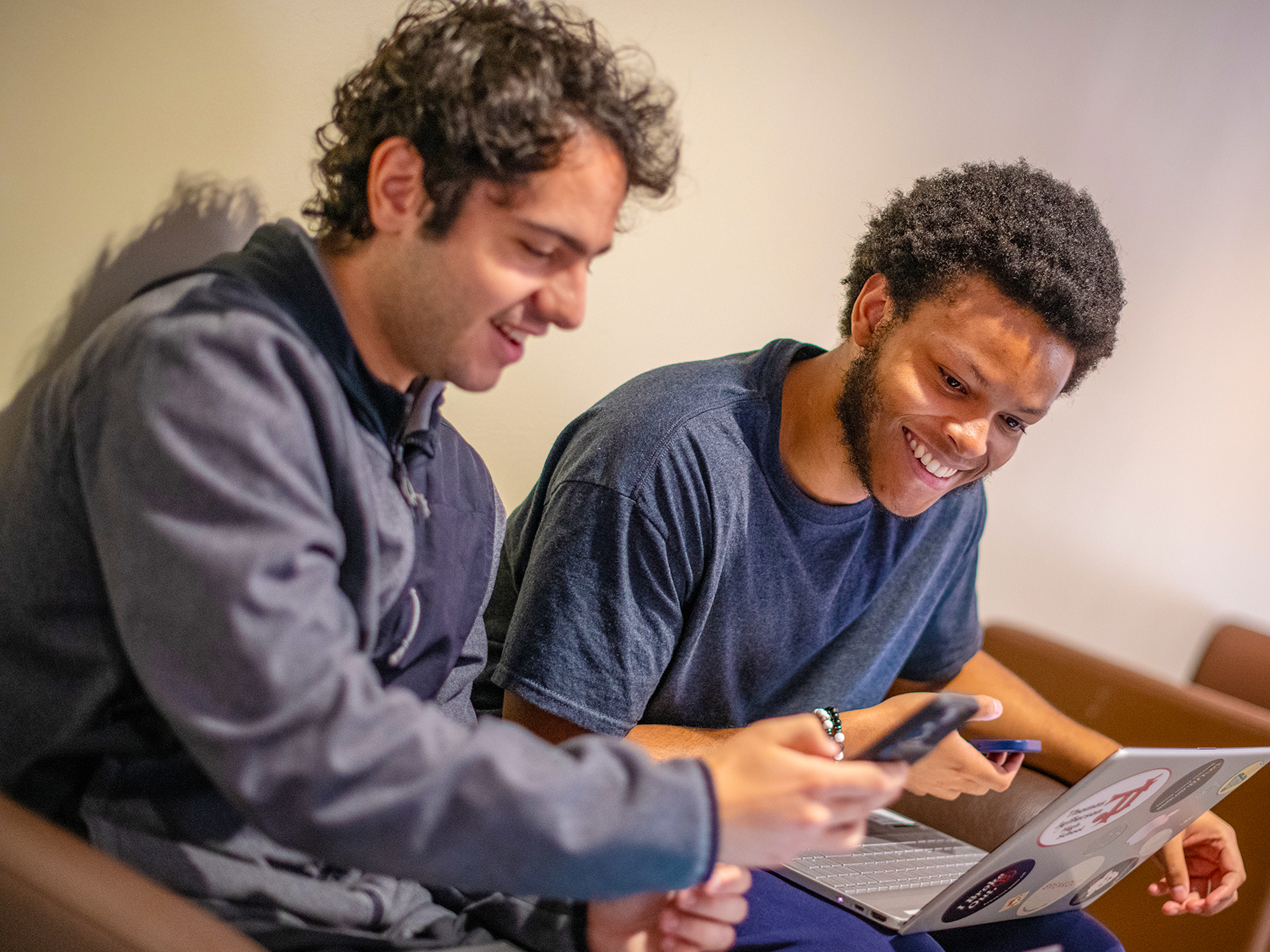 Two students looking at a phone and laptop sitting together