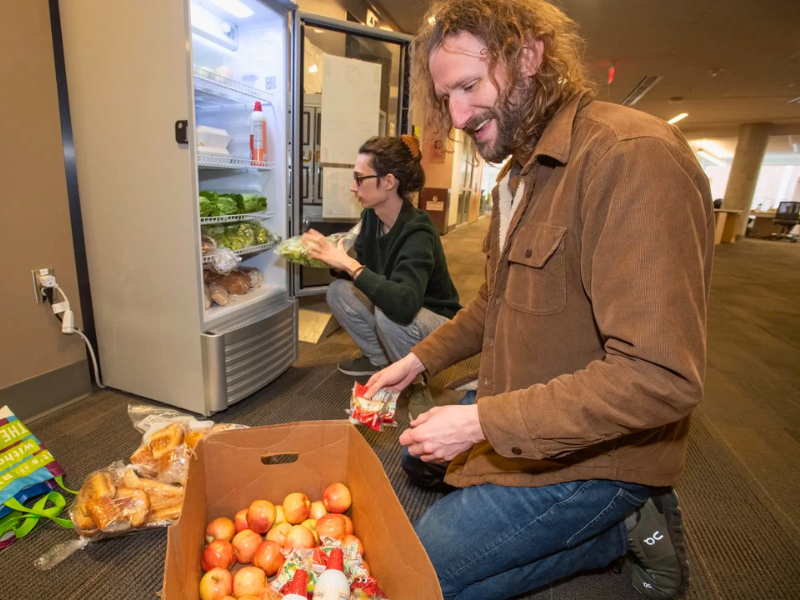 Two people stocking a fridge with fresh foods.