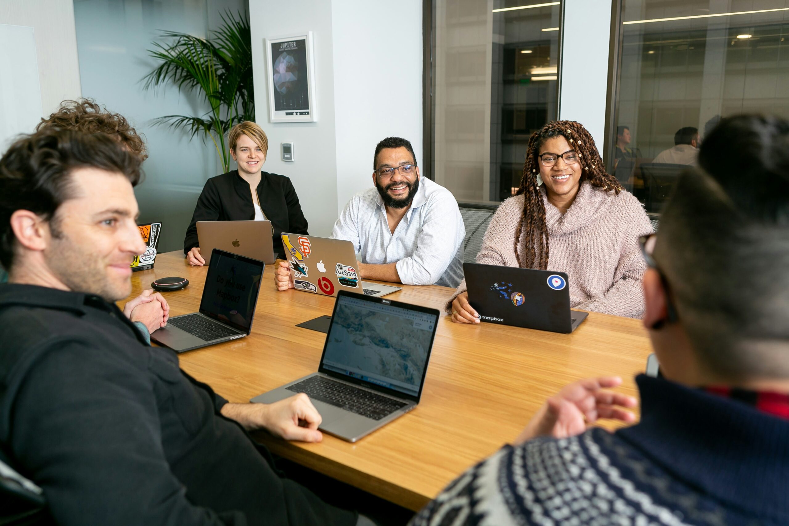 Photo of people sitting around a desk with laptops and engaging in conversation.