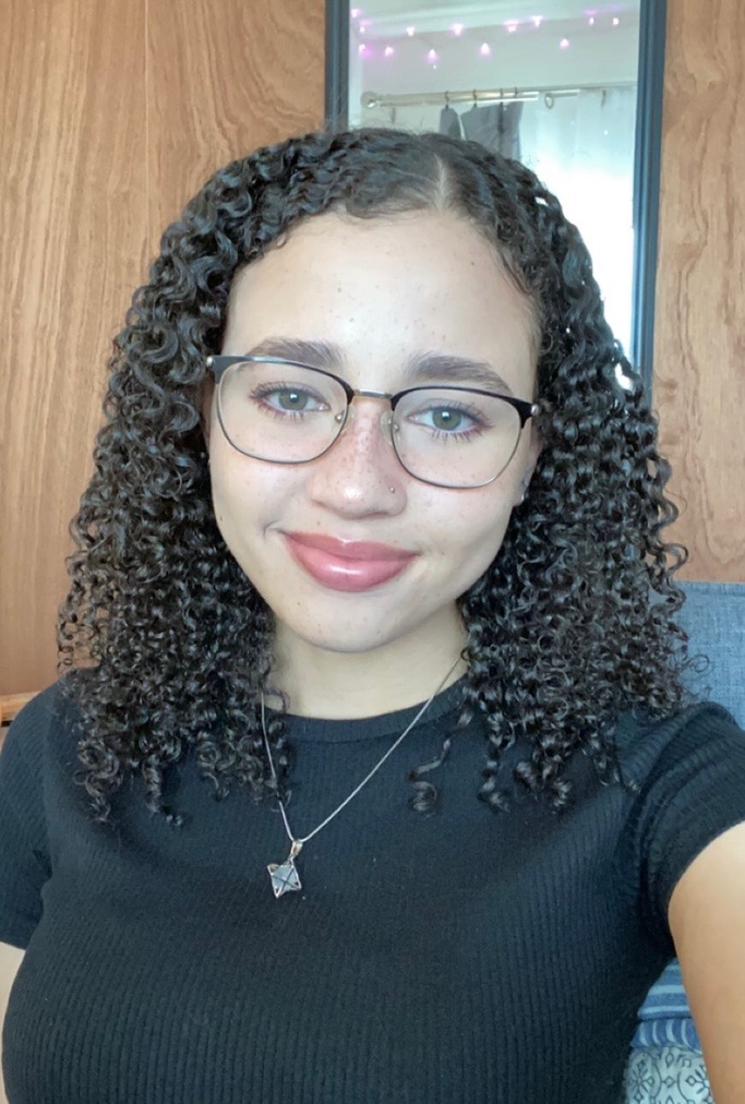 A selfie of Gabrielle Levy smiling. She has dark curly hair and glasses.