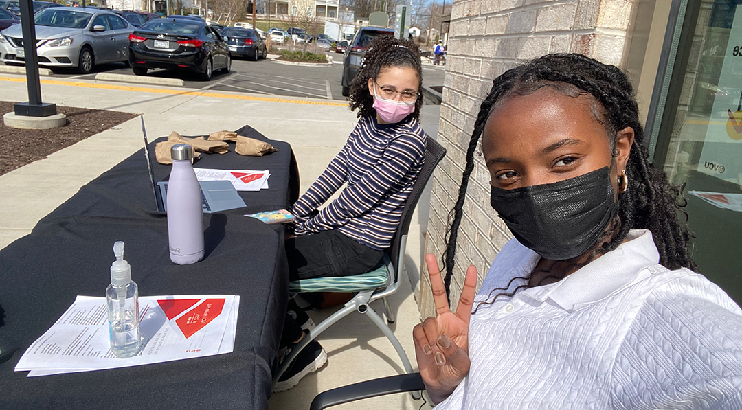 Selfie of two girls, Gabrielle Levy and Victoria Chege, tabling outside of the VCU Health Hub at 25th. Both girls are masked and Chege holds up a peace sign.