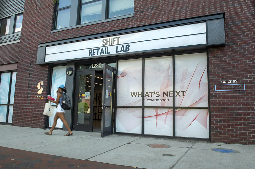 A person walking in front of a retail store front. On top of the doorway there is a marquee that says shift retail lab.