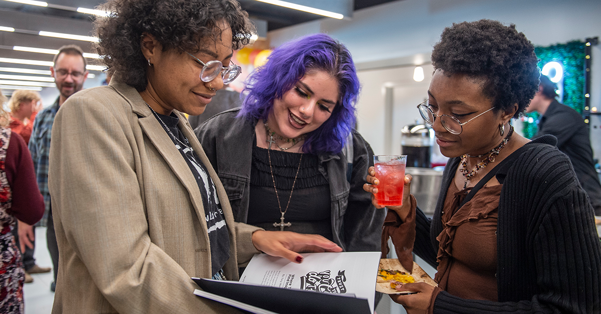 3 students looking at a magazine during the launch party of it's publication.