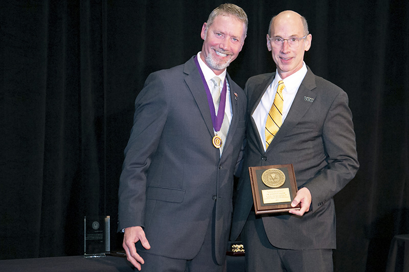 American College of Prosthodontists President Dr. Lars Bouma posing with Dr. Lyndon Cooper who holds a plaque for his 2022 Dan Gordon Lifetime Achievement Award.