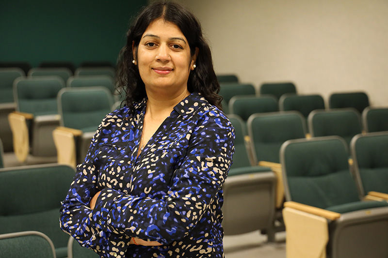 Dr. Shillpa Naavaal poses in front of a row of chairs in a lecture hall. 