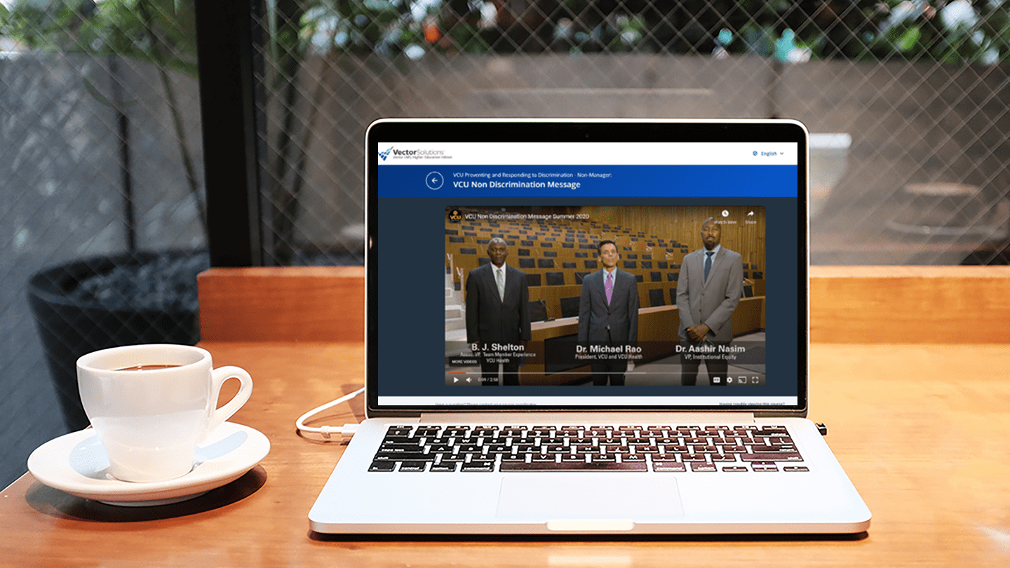 A laptop on a table with a cup of coffee to the left. On the laptop is VCU's non-discrimination training.