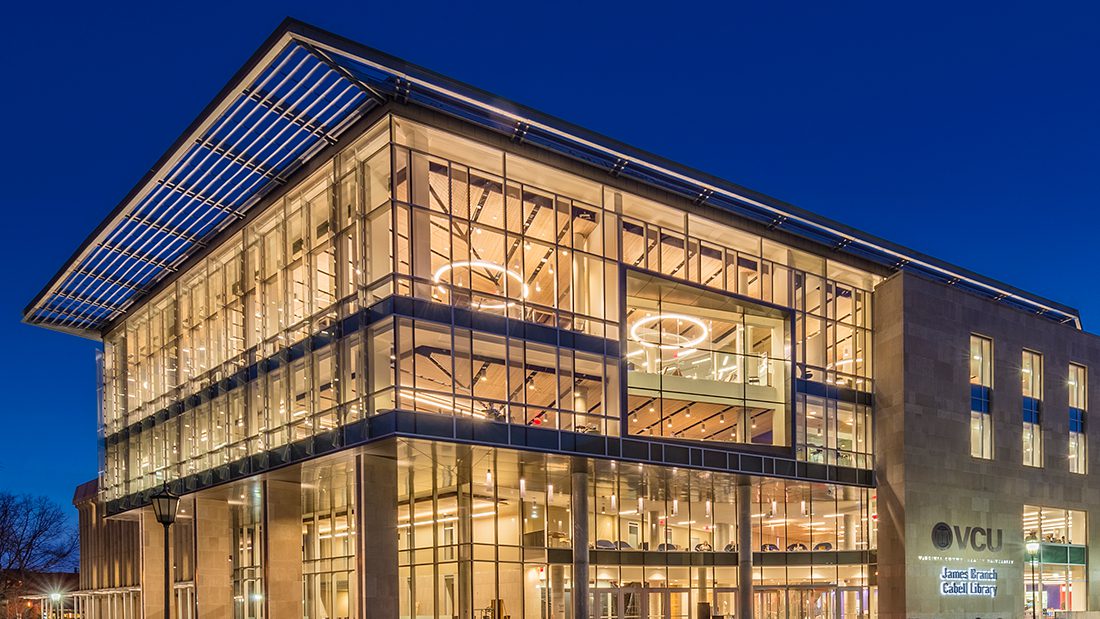 The V-C-U James Branch Cabell Library lit up at night against a dark blue sky.
