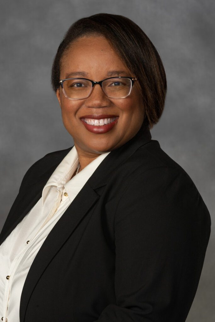 Professional headshot of a woman wearing glasses, a white button-up and black suit jacket.