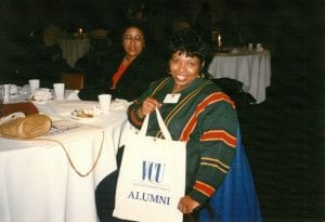 A woman smiling at the camera holding a VCU Alumni branded tote bag.
