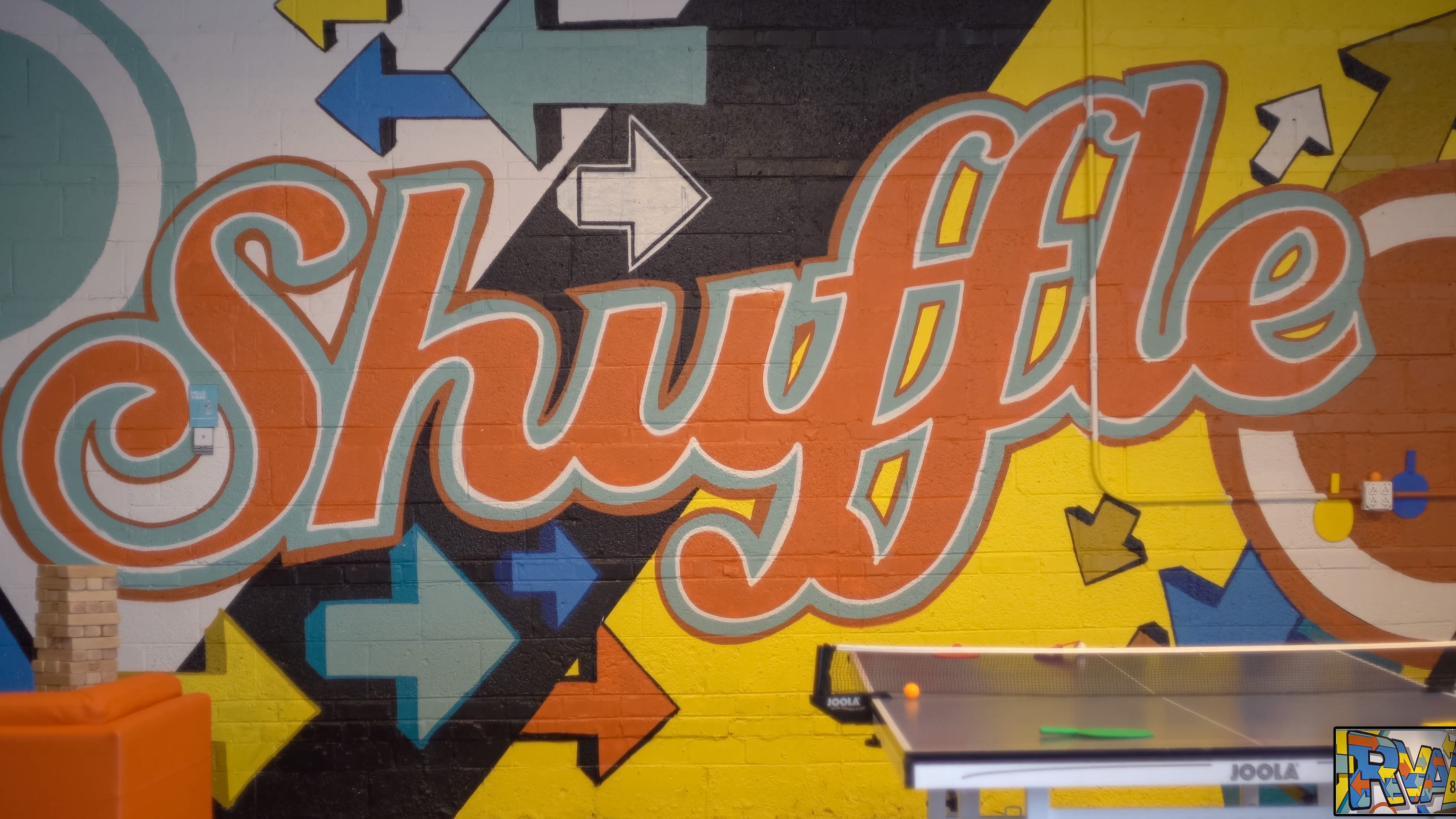 A wall mural that says "Shuffle" in a script font, surrounded by multicolored arrows.