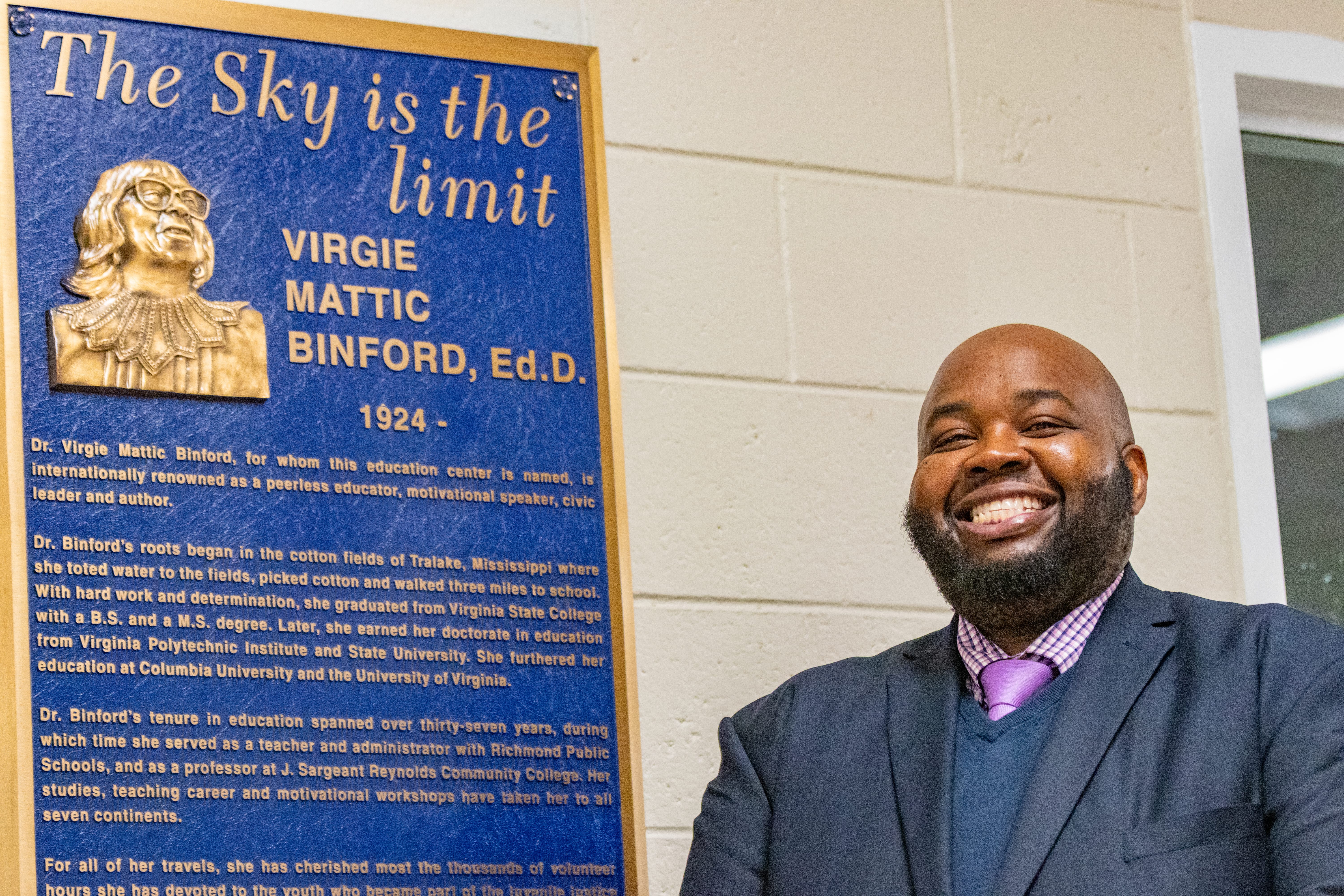 Rodney Robinson stands beside a sign that details the biography of Virgie Binford, Ed.D., for whom the education center where he teaches is named.