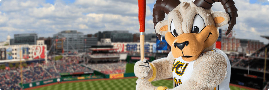 VCU's mascot Rodney the Ram stands in front of a baseball diamond, holding a bat at the ready.