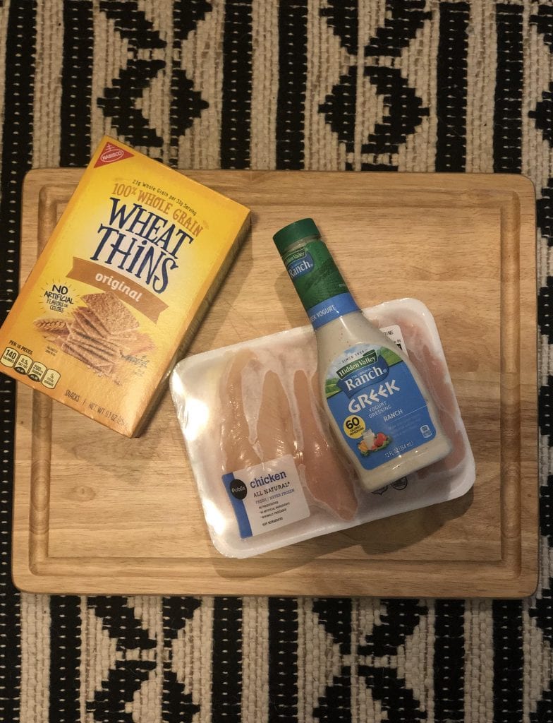 A box of crackers, chicken tenderloins and Ranch dressing on a wooden cutting board.