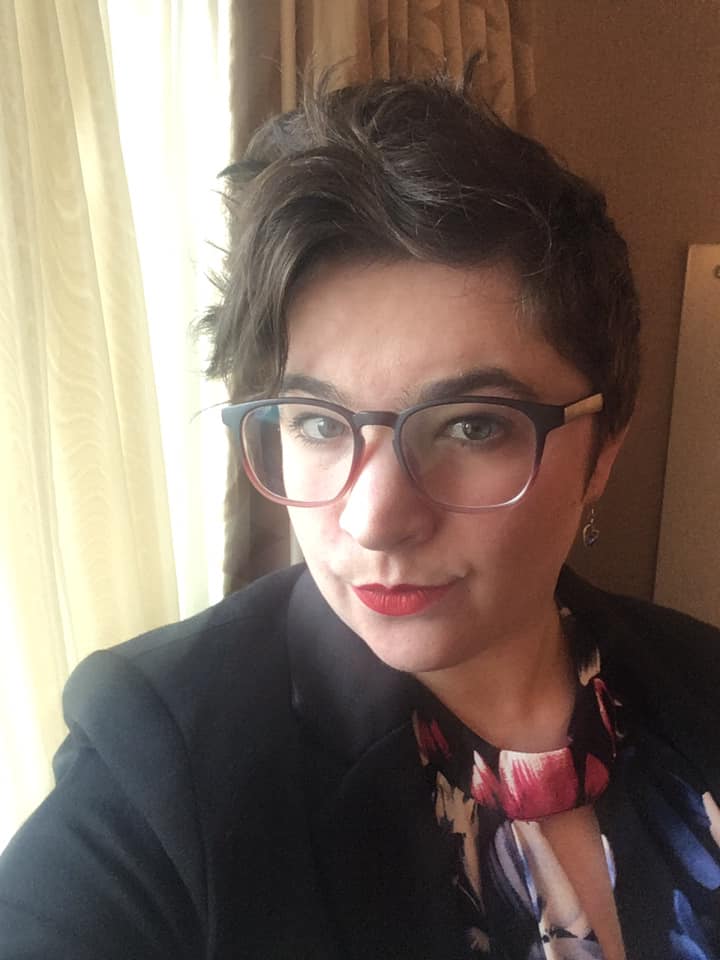 An image of Nyssa Towsley, a white person with short brown hair, wearing red glasses.