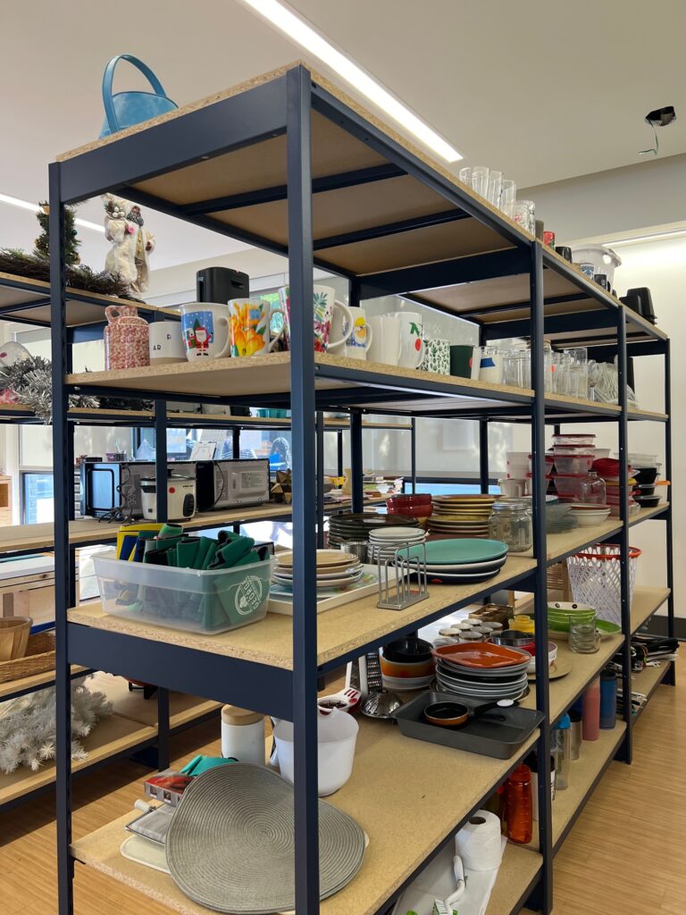 Tall metal shelves, full of plates and mugs and home decor items, stand in a room at the VCU Free Store.