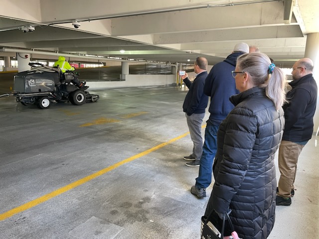 Several employees from VCU Parking & Transportation watch a street sweeper cleaning the ground on one level of a parking deck.