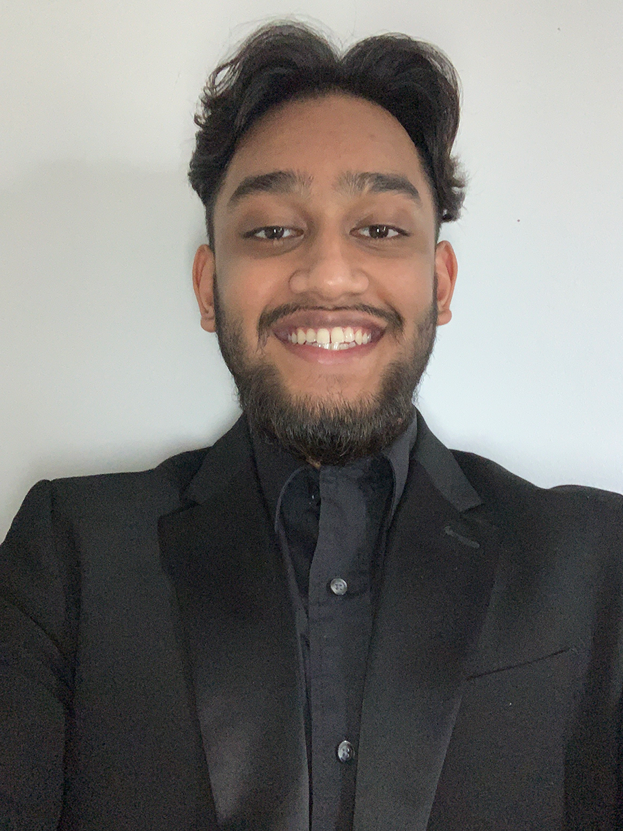 Hasib Zaman smiling broadly in an all black suit against a white background.