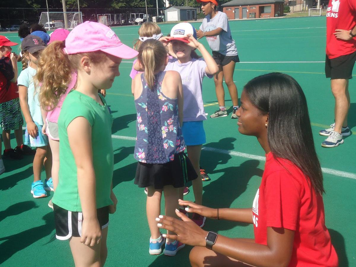 Cameron Mattex crouches on a tennis court to speak with a youth tennis program participant.