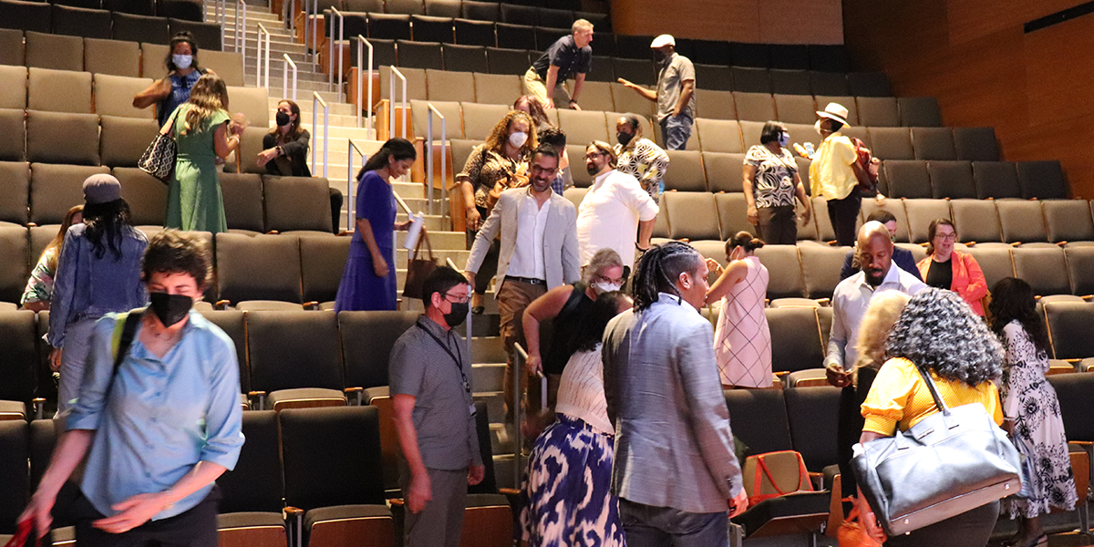 iCubed members socialize after their annual meeting. They gather in a large auditorium.