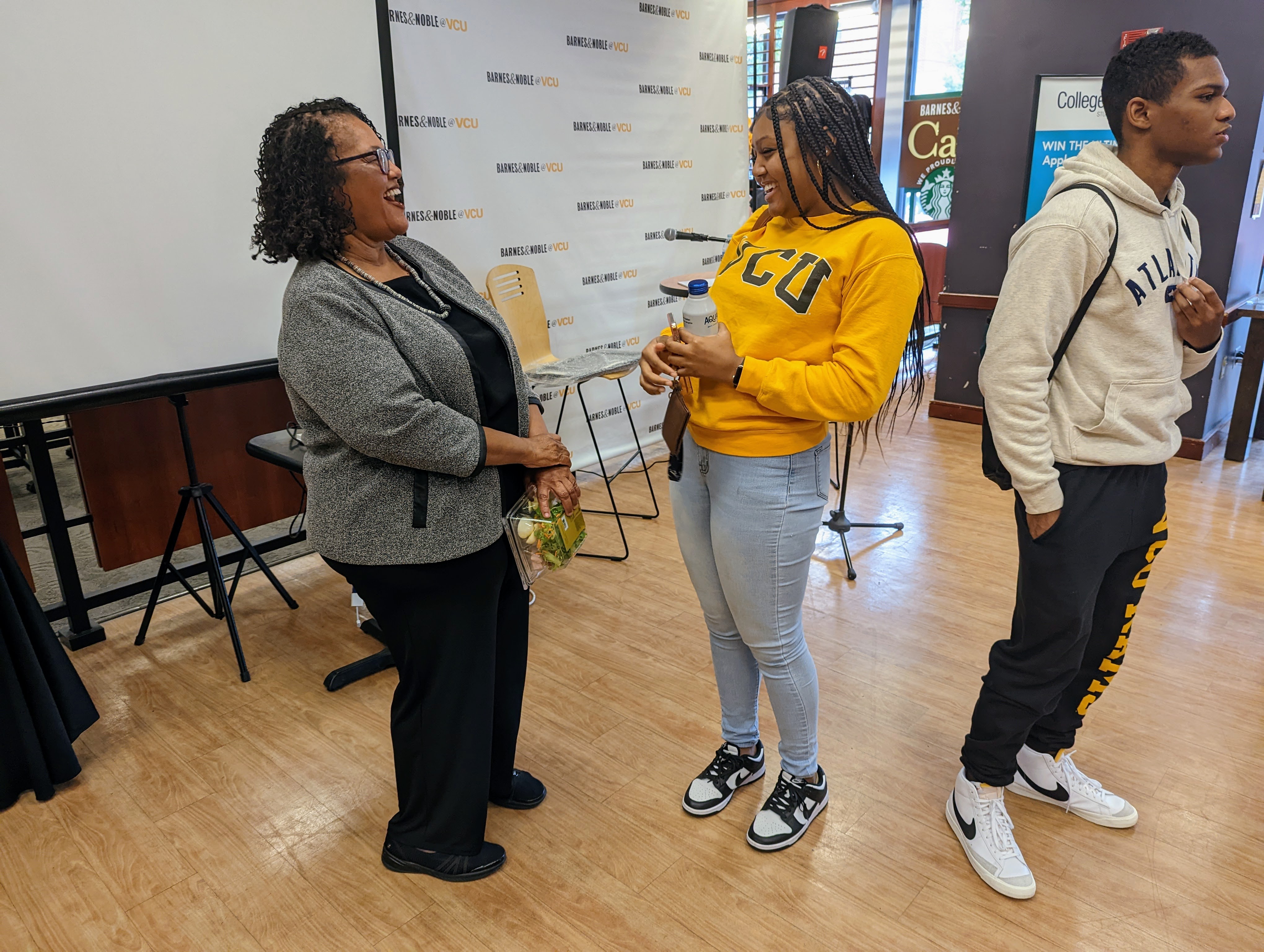 Dr. Belgrave laughs with a young person who attended her talk, presumably a student, Belgrave wears professional dress while the student wears a bright yellow and black VCU hoodie.