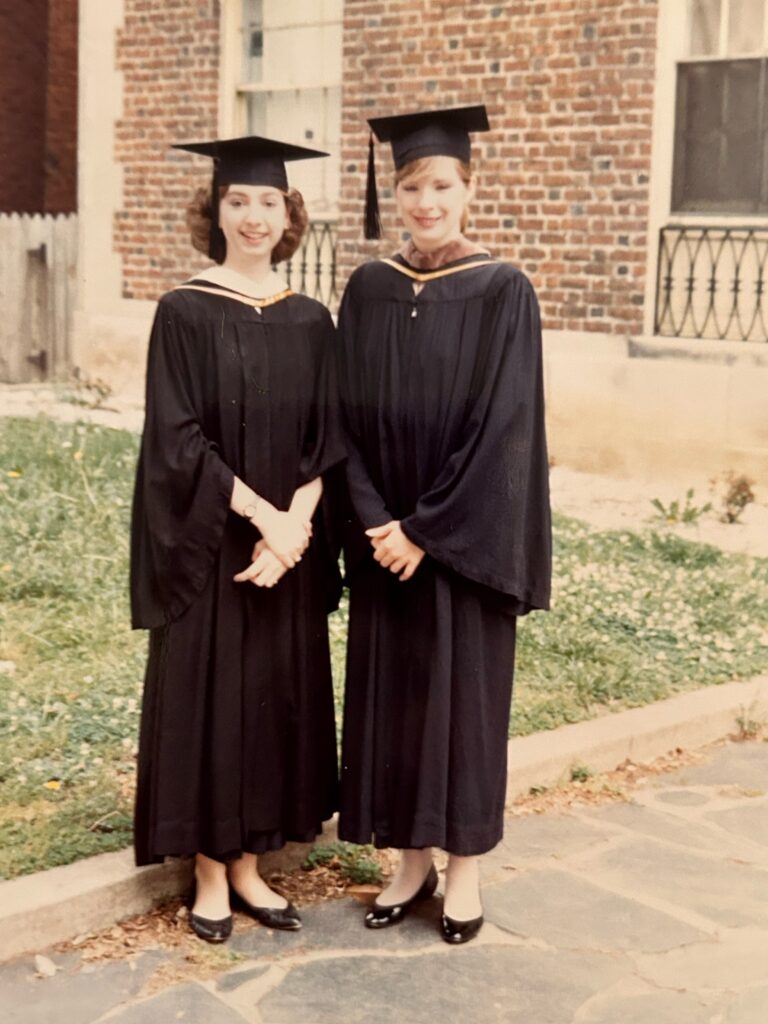 Two women in regalia posing outside an apartment. 