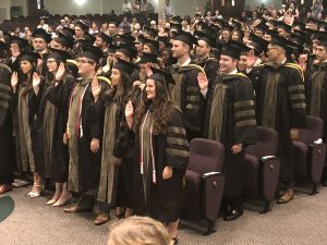 Students in regalia stand with right hands raised as they take the Oath of a Pharmacist.