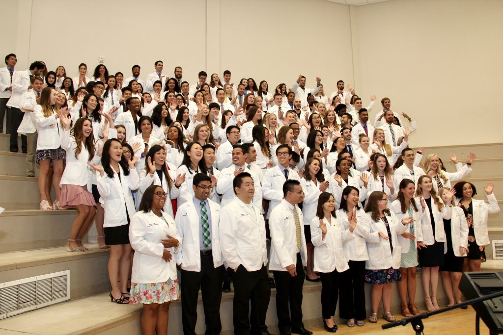 Members of the V C U Pharmacy Class of 2022 stand in a group, wearing the white coats.