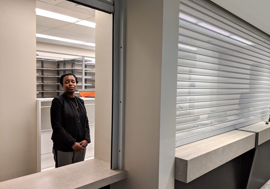 Woman stands in an empty office. She is framed in a window.