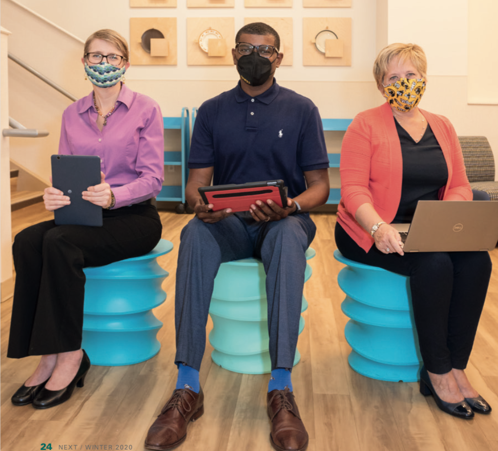 Three masked people sit and hold computers