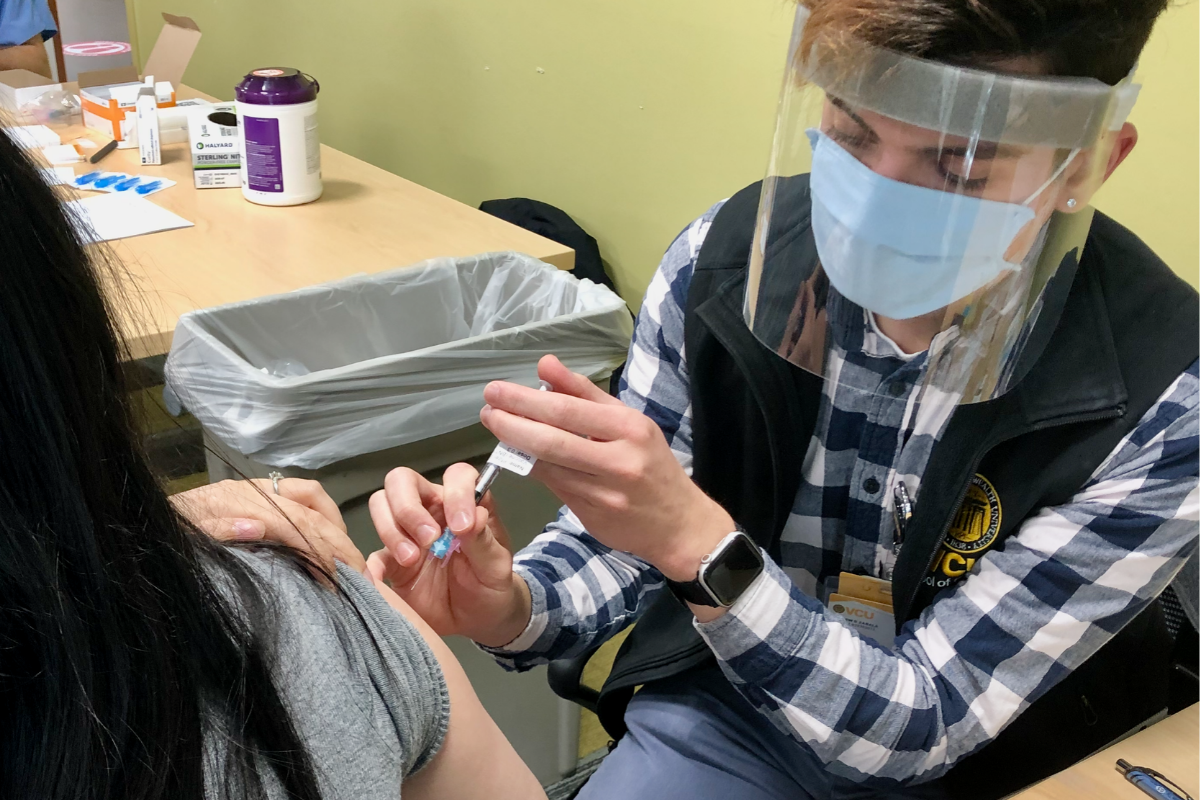 A person in a surgical mask and face shield gives a vaccination with a syringe.