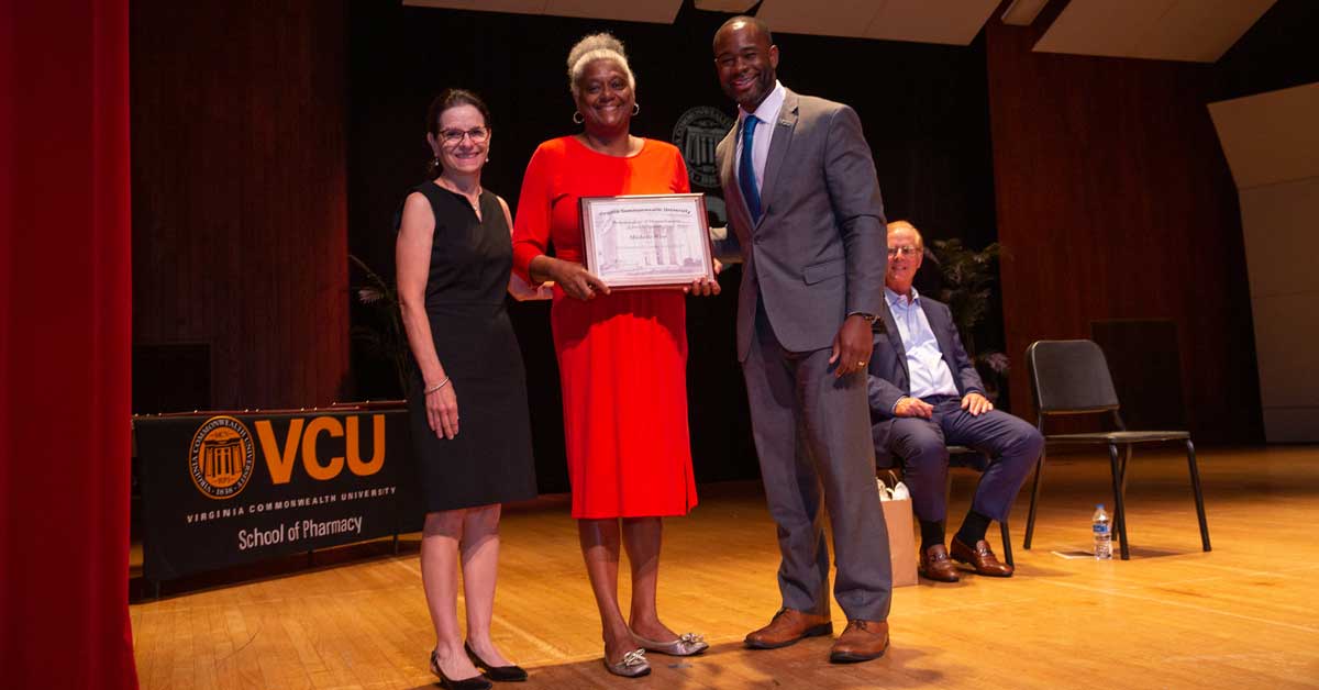 dean ogbonna and cindy kirkwood give a staff award to a school of pharmacy employee