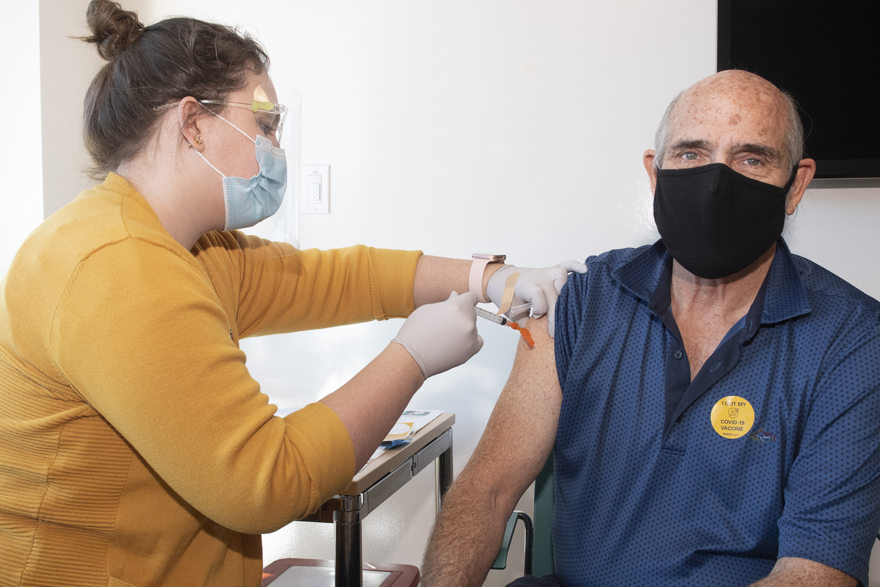 An older adult looks toward the camera while a student vaccinates him against COVID-19 at the VCU Health Hub at 25th.