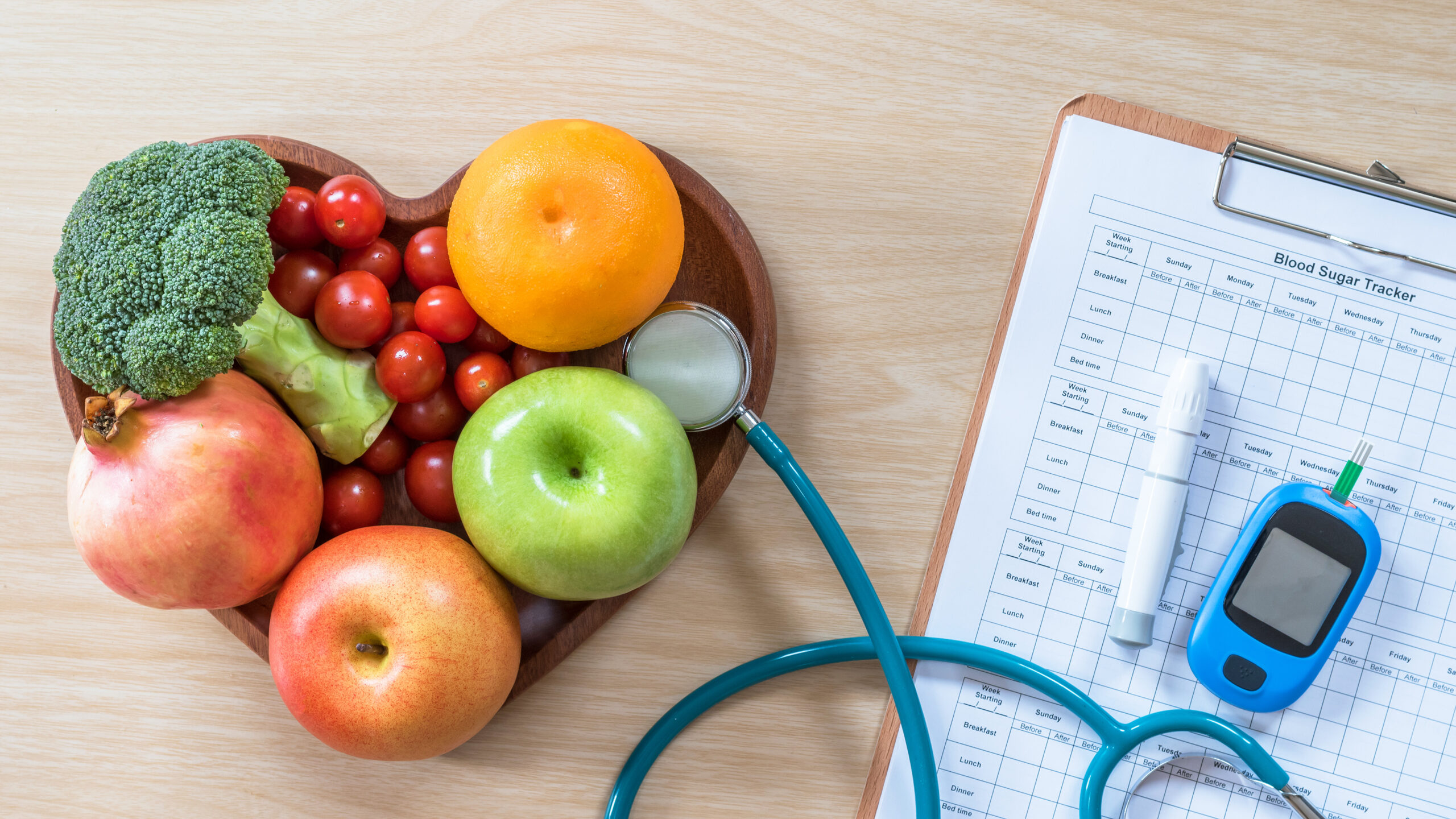 A photo with fruit in a heart-shaped bowl next to a stethoscope and blood sugar monitor.