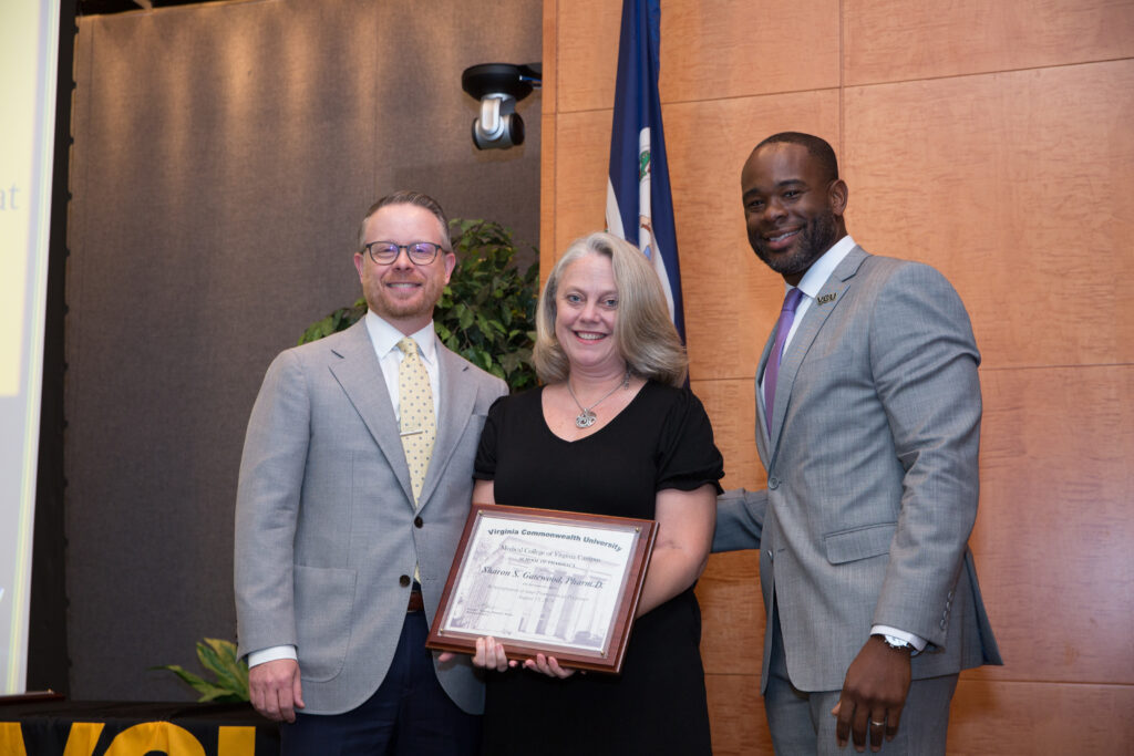 Sharon Gatewood, a woman in a dress holding an award, smiles for a photo flanked by two smiling men in suits