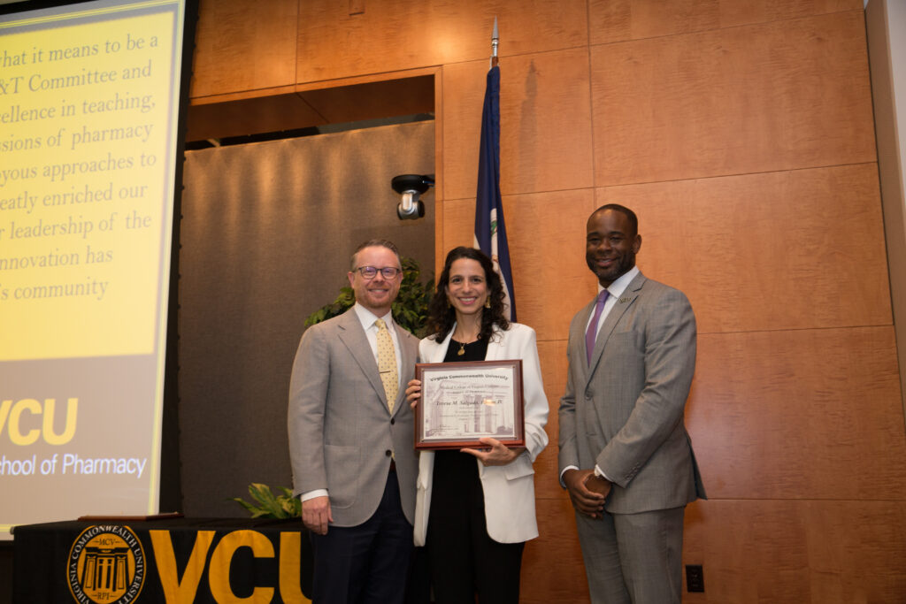 Teresa Salgado, a woman in a pantsuit holding an award, smiles for a photo flanked by two smiling men in suits