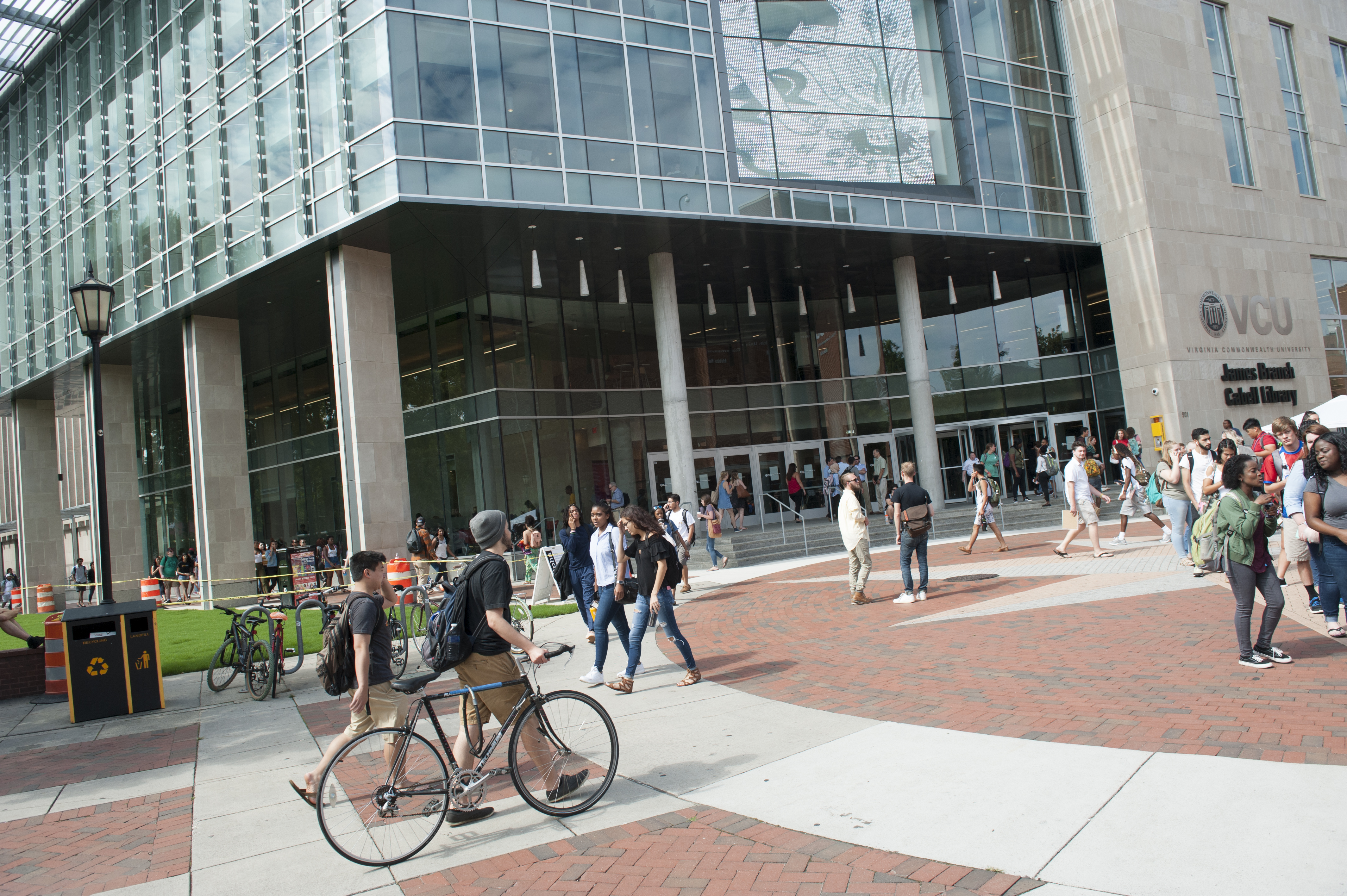 Students are walking, riding bikes and chatting on the first day of class at VCU. Cabell Library is in the background.
