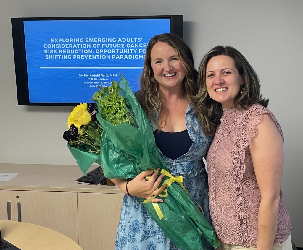 Image of two people standing in front of a TV screen