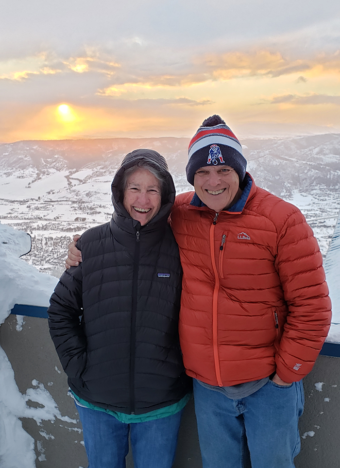 Deborah and Ira Colby, smiling; the landscape behind is a snow-covered mountain with the sun setting.