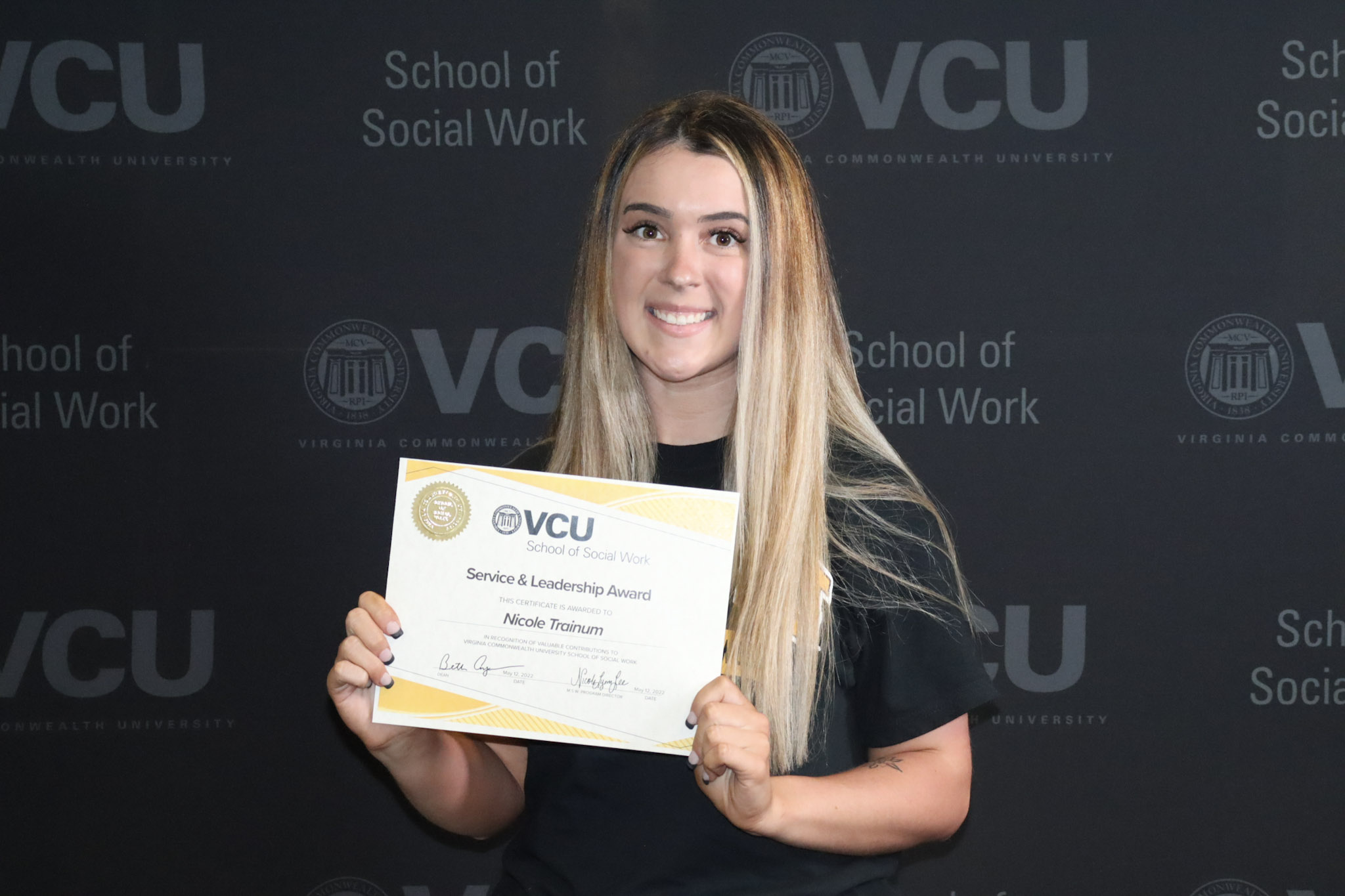 A student poses with awards certificate in front of VCU School of Social Work backdrop