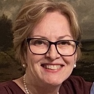 Headshot of Marjorie Stuckle, smiling, wearing glasses and a pearl necklace.