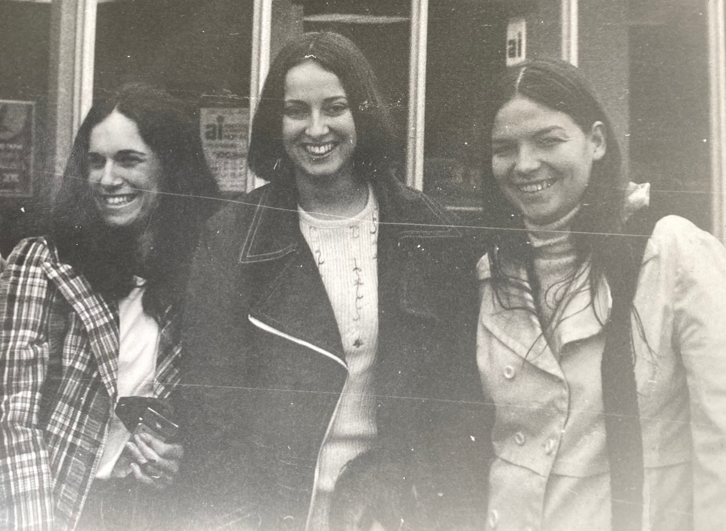 Marjorie Stuckle stands with two other students, all smiling, in a black-and-white photo from 1973. The student at left is wearing a checked jacket and white top; Stuckle is wearing a dark jacket and white top; and the third student is wearing a light colored trench coat over a light turtle neck. 