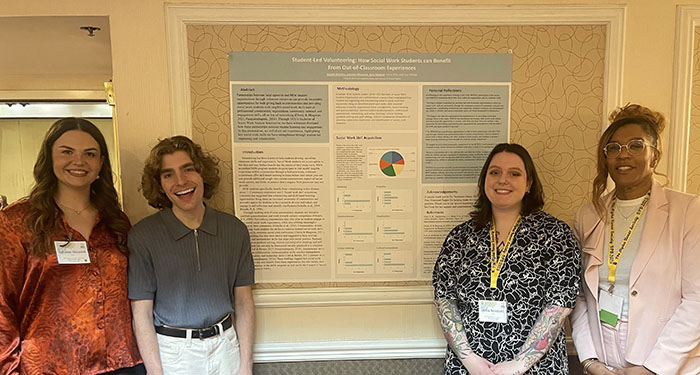 Four people stand in front of a poster titled Student-Led Volunteering: How Social Work Students can Benefit from Out-of Classroom Experiences.