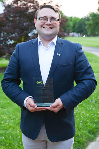 Person stands smiling and holding a glass award.