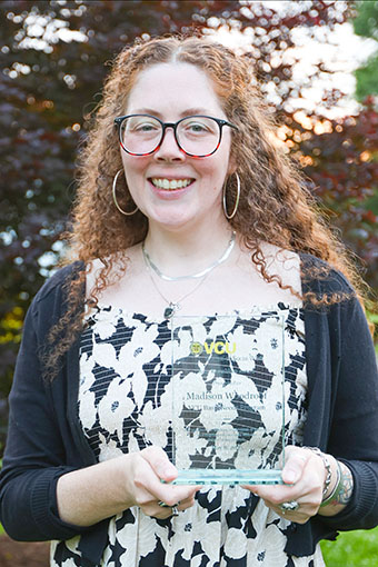 Person stands smiling and holding a glass award.