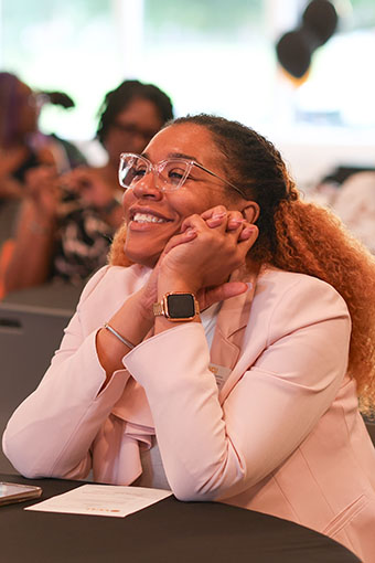 A person sitting with clasped hands and smiling.