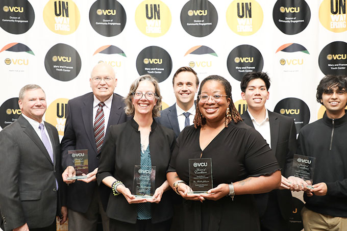 A group of seven people standing with awards. In the background are graphics that say VCU Division of Community Engagement and "Unwavering."