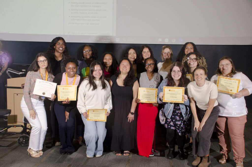 Sixteen people pose stand in a group, some holding award certificates.