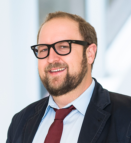 headshot of Andrew Barnes in a light shirt with maroon tie, dark jacket and black square glasses